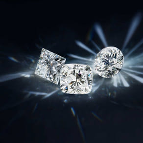 Three sparkling cut diamonds against a dark background with radiant light reflections.